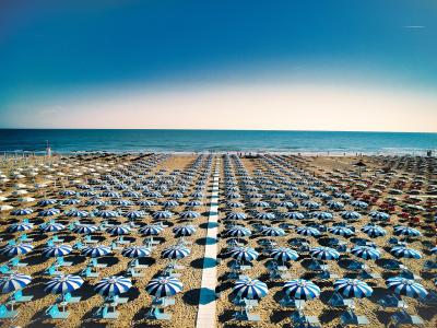 Plage avec parasols bleus et blancs alignés, vue sur la mer.