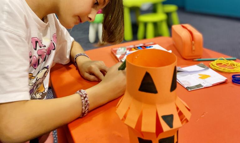 Girl making Halloween decorations with orange paper and markers.